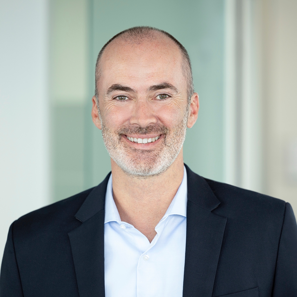 Mann in Anzug mit freundlichem Lächeln steht in modernem Büro.